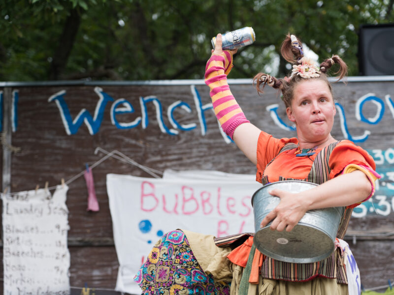 A washing well wench holds up a beer for the audience.