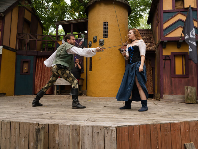 A man and woman have a sword fight on a renaissance faire stage