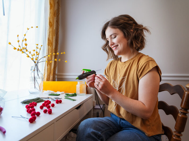 A woman looks down at her glue gun while making felt holly bunches.