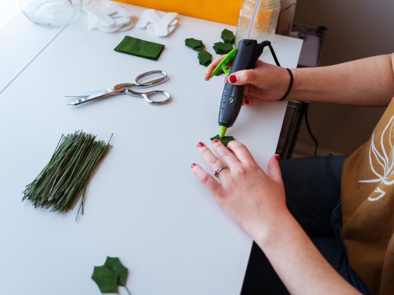 Hands hot glue green felt holly leaves.