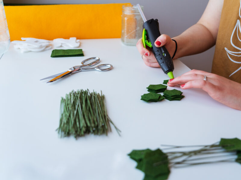 Hands hot glue green felt at a desk.