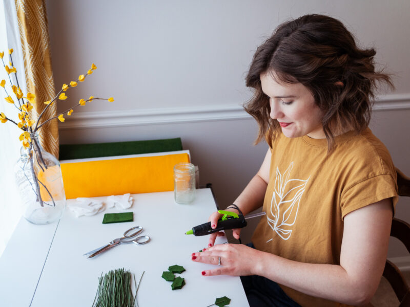 A woman makes felt holly bunches at a desk.